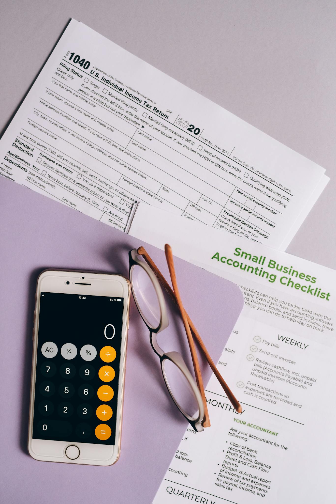 Flat lay of tax forms, checklist, smartphone, and glasses for small business accounting.