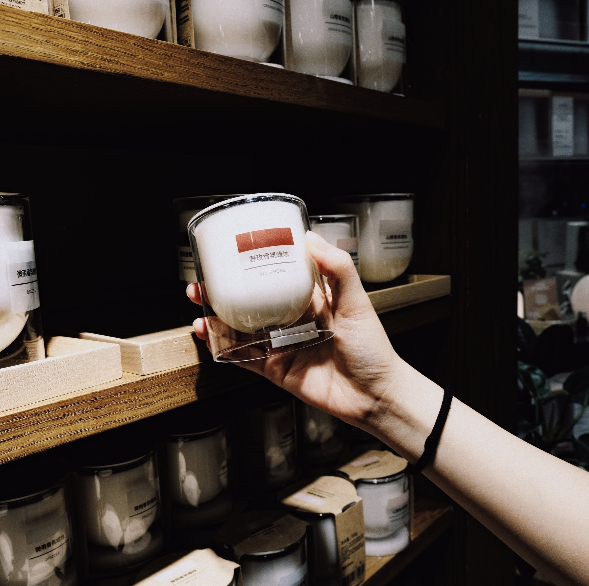 A hand picks a scented candle from a shelf in a dimly lit store interior.